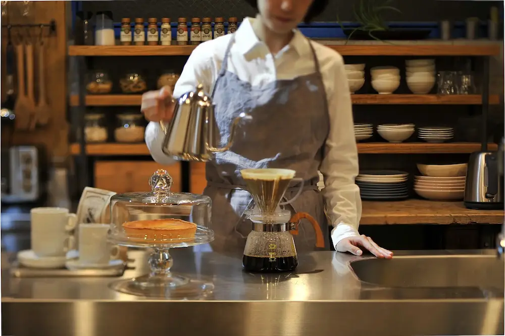 みみずく洋菓子店の世界観を表現した店内風景。スタッフがコーヒーをドリップする温かなシーン。